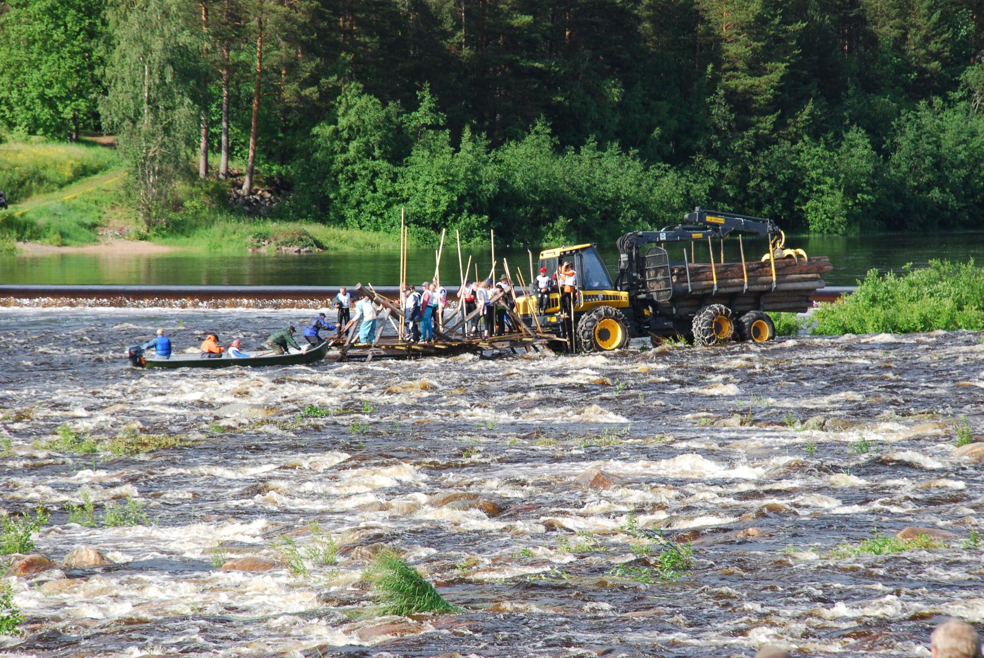 Tukkilaiskisailijoita seisoo metsäkoneen kyydissä valmiina laskemaan koskea.